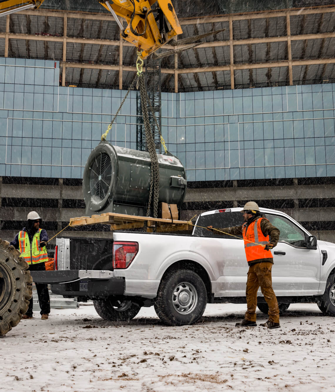 Construction workers load heavy equipment onto a white Ford pickup truck